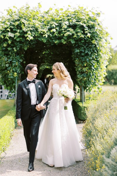 Bride and groom walk the pathway to garden holding hands