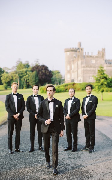 groom and groomsmen stand on pathway in black suits