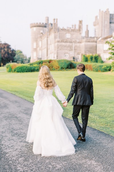 Bride and groom walk along the pathway to wedding venue