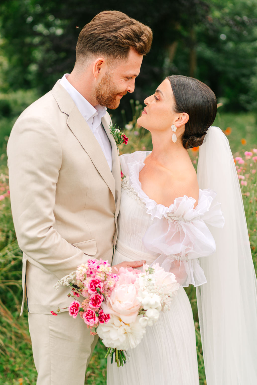 Bride and groom smile in garden park long grass facing each other