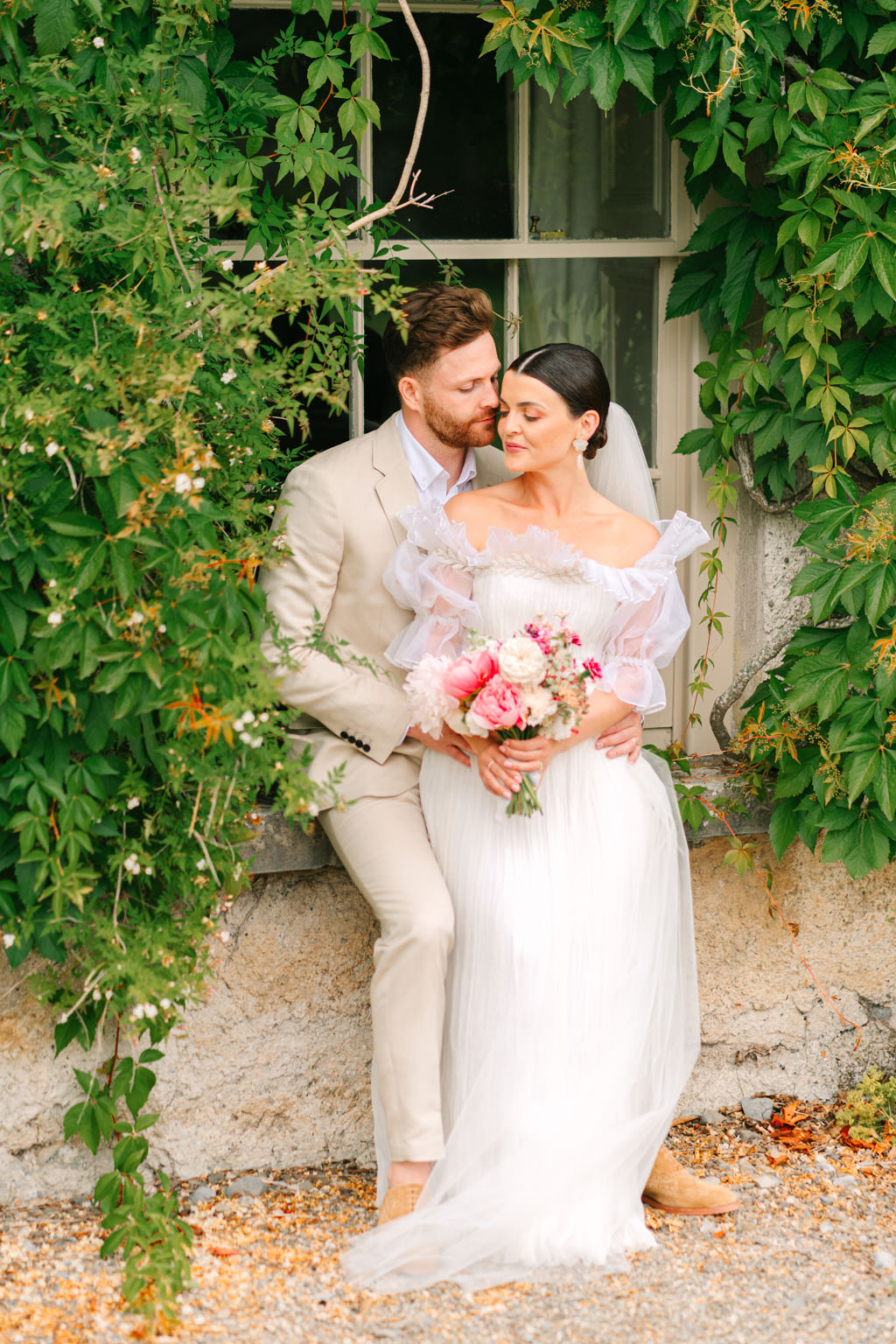 Bride and groom lean against bricked wall and smile