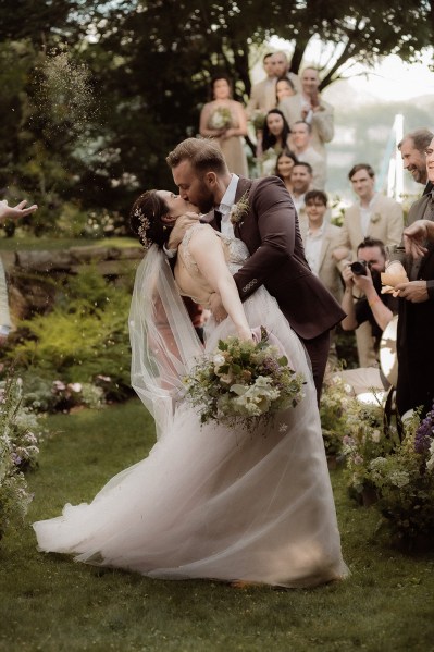 Bride and groom kiss he leans bride over in front of guests she holds bouquet