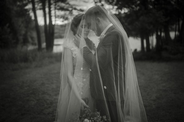 Black and white image of bride and groom standing in grass/park