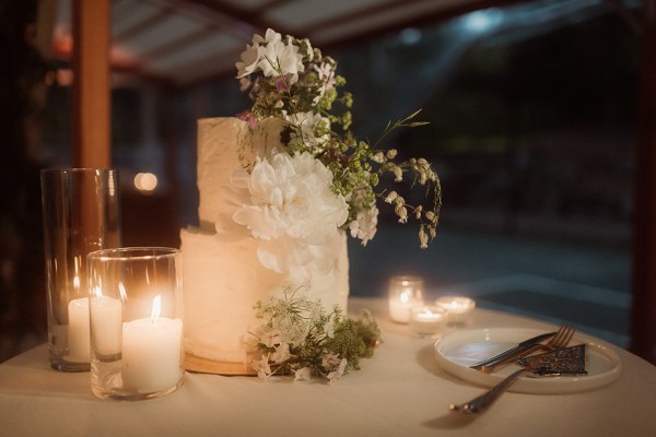 White wedding cake covered in white flowers candles lit