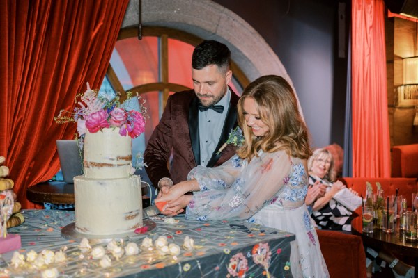 Bride and groom cutting the cake pink flowers on top lit candles