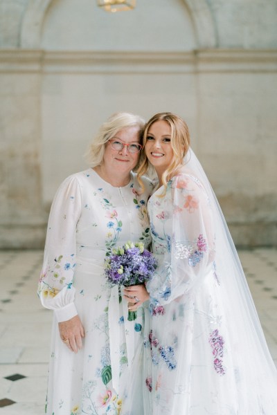 Bride and mother hug purple bouquet flowers