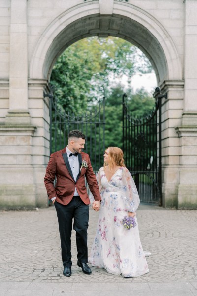 Bride and groom walking in courtyard archway in background