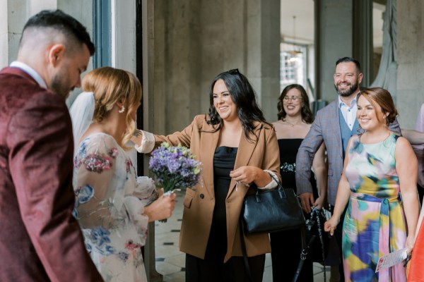 Guest goes in to hug bride holding purple bouquet flowers