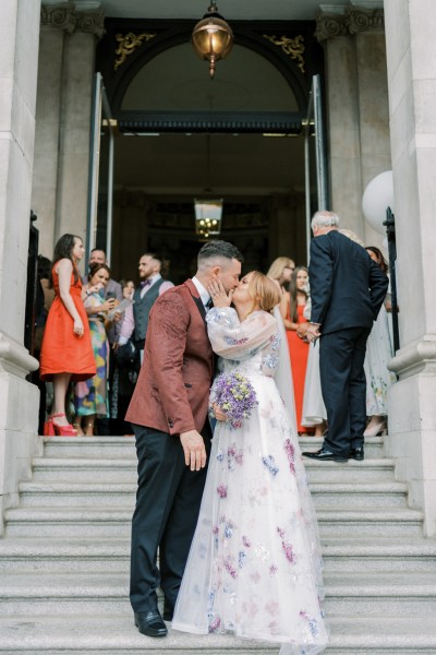 Bride and groom standing on steps guests behind them