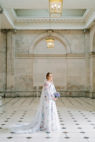 Bride standing on the black and white tiles holding bouquet purple