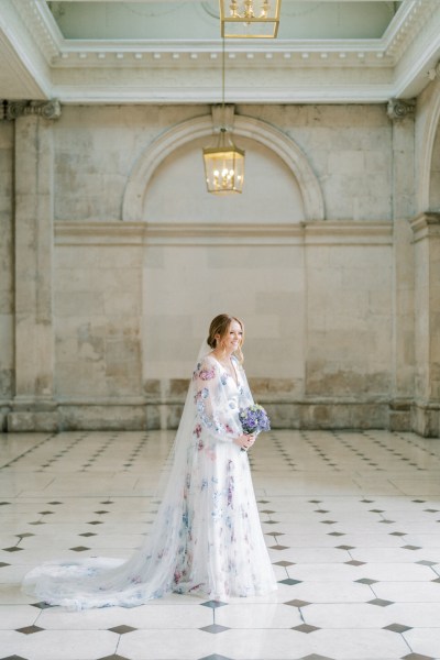 Bride standing on the black and white tiles holding bouquet purple