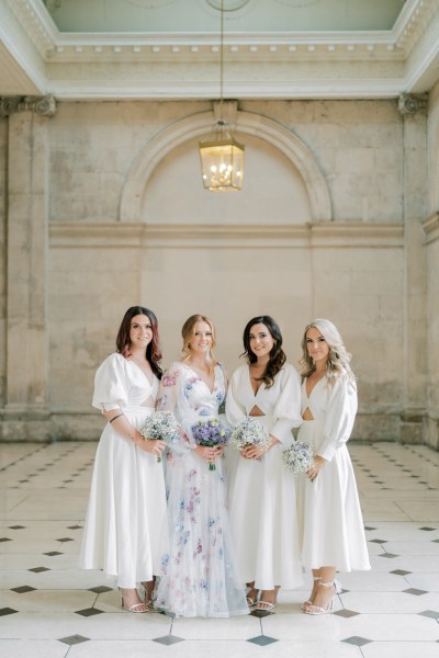 Bridesmaids and bride stand on the white and black tiles in white dresses, floral gown