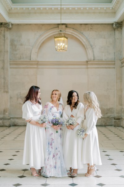 Bridesmaids and bride stand on the white and black tiles in white dresses, floral gown