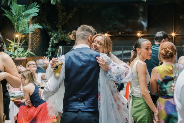 Groom hugs bride as she holds bottle of beer