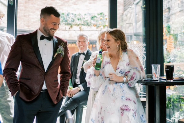 Bride laughs holding glass of beer with groom smiling