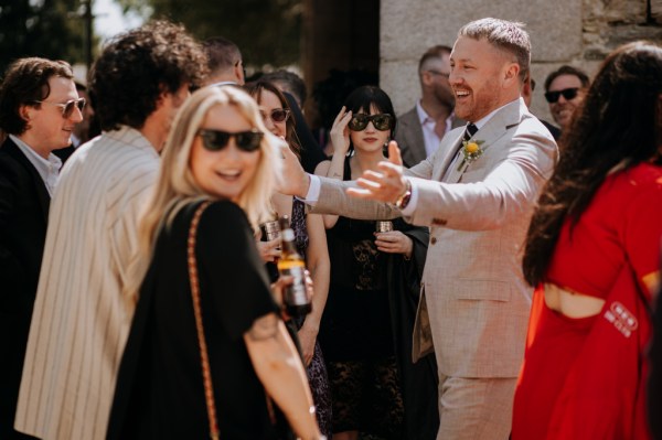 Blonde woman smiles at camera groom goes in to hug man