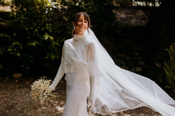 Bride stands veil blowing in the wind