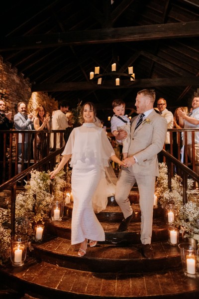 Nighttime shot of bride and groom surrounded by candles clapping guests