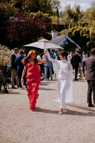 Bride puts her hands up in the air with woman wearing red dress