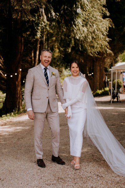 Bride pulls up her veil as she walks with groom linked arms