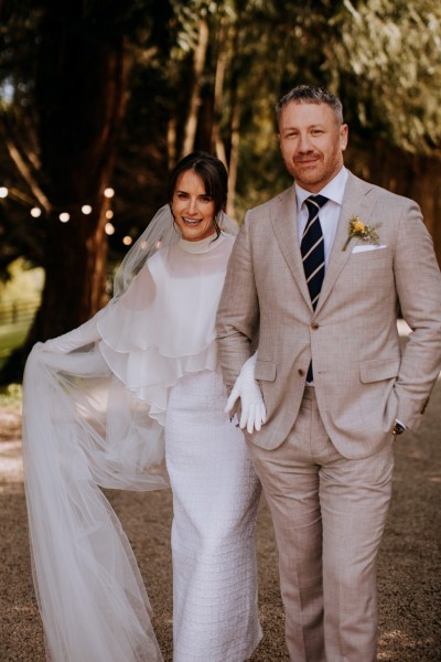 Bride pulls up her veil as she walks with groom linked arms