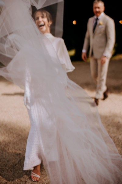 Brides veil blowing in the wind groom in background