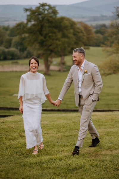 Bride and groom walk on the grass together holding hands