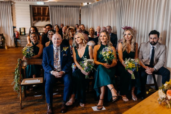 Bridesmaids sit in front row smiling with father seated