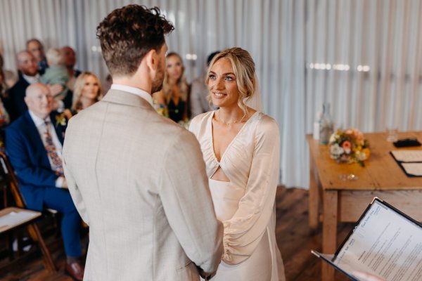 Bride and groom stand holding hands at alter reading out vows