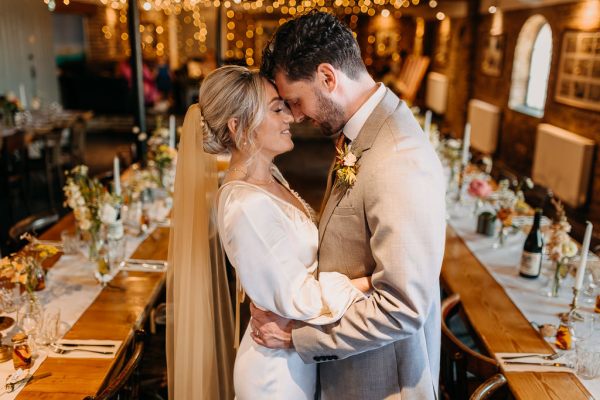 Bride and groom hold heads together in wedding reception room