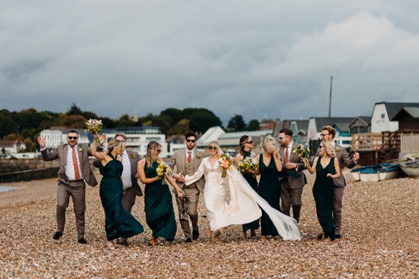 Bride groom bridesmaids groomsmen celebrate wedding on the beach sand rocks and sea veil blowing in wind