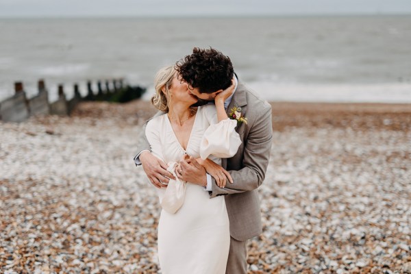 Beach setting bride groom on the sand kissing over the shoulder