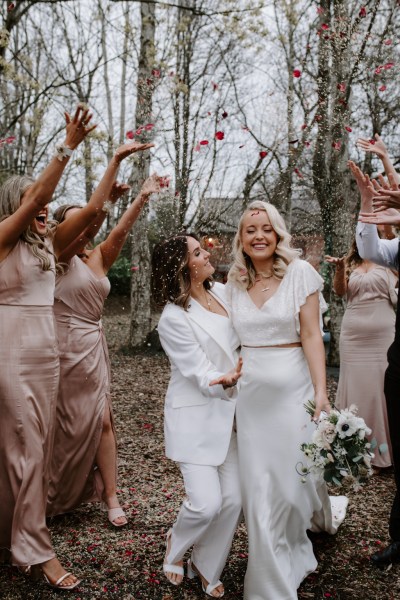 Brides walk under confetti being thrown on them by guests