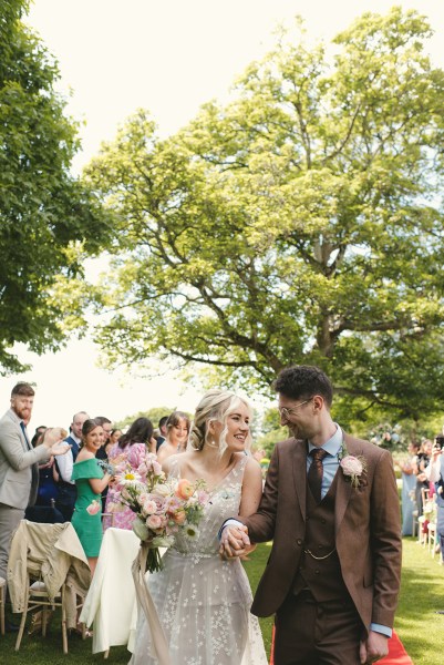 Bride and groom exit ceremony in front of guests holding each other