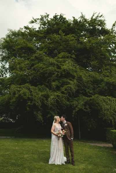 Bride and groom stand in the garden together trees in background