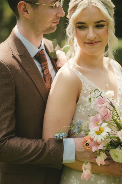 Bride and groom smile holding bouquet flowers in garden