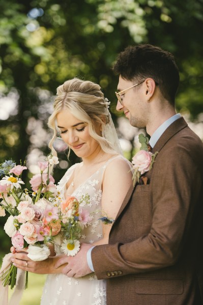 Bride looks down as groom hugs her from behind