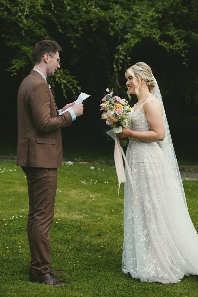 Bride and groom stand in the garden together they read their vows