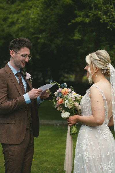 Bride and groom stand in the garden together they read their vows