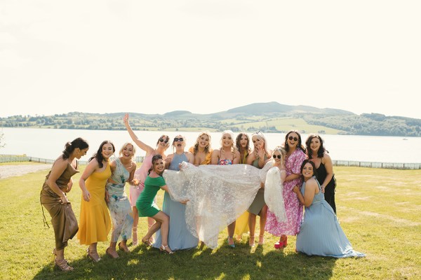 Atmosphere shot colourful dresses guests hold up bride mountains in background