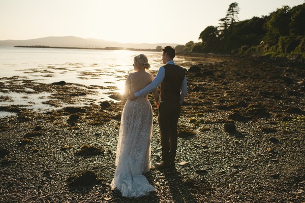 Bride and groom in beach setting sunset behind couple they face the sea behind