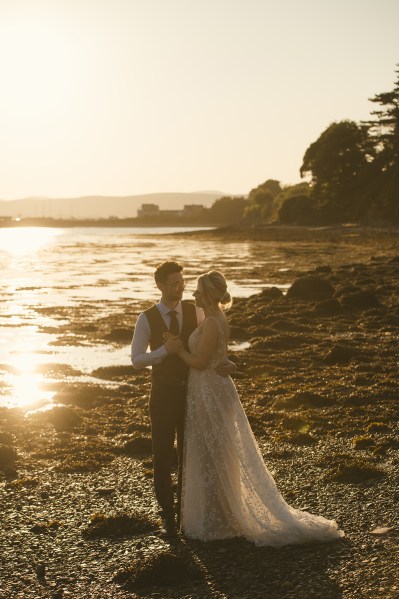 Bride and groom in beach setting sunset behind couple they embrace