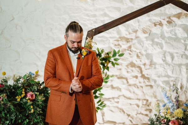 Groom stands at alter cupping hands together