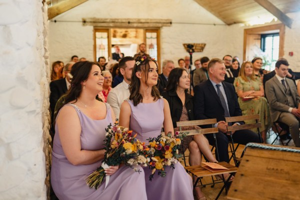 Two bridesmaids in purple lilac dresses sit during ceremony