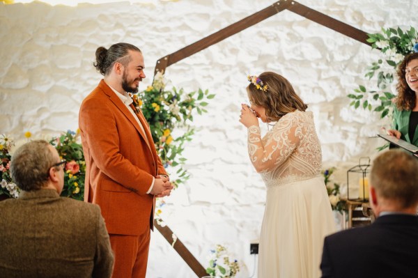 Bride drinks glass of wine as groom watches