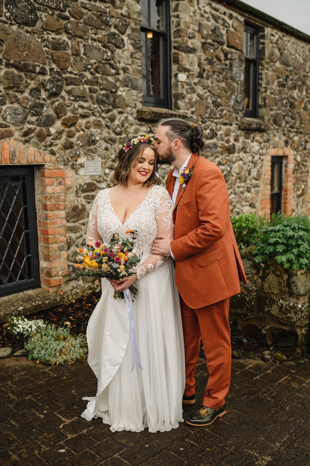 Groom kisses bride on the forehead exterior shot as she smiles