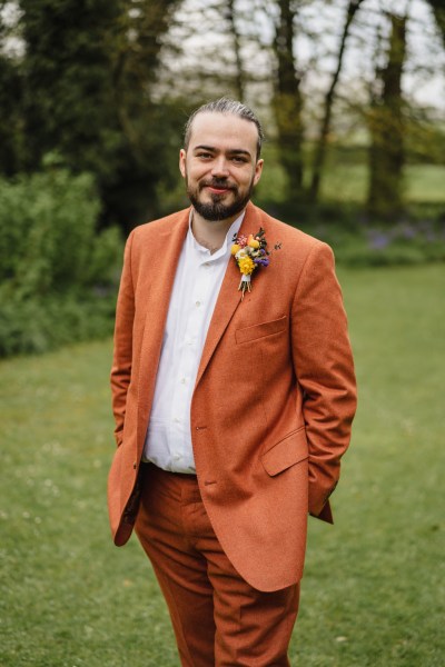 Groom in orange suit focus is on orange pin brooch