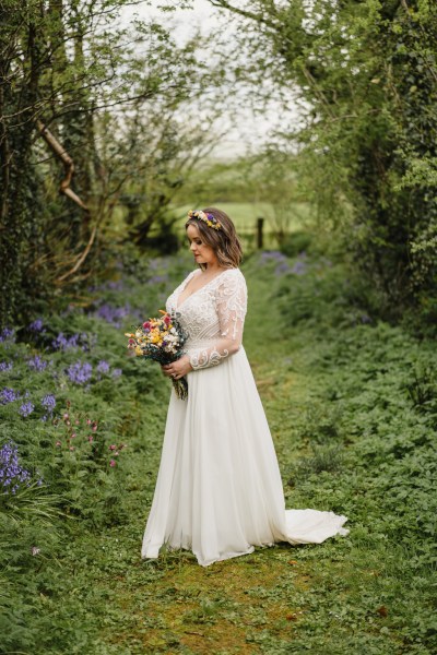 Bride on her own stands on the green grass in forest setting