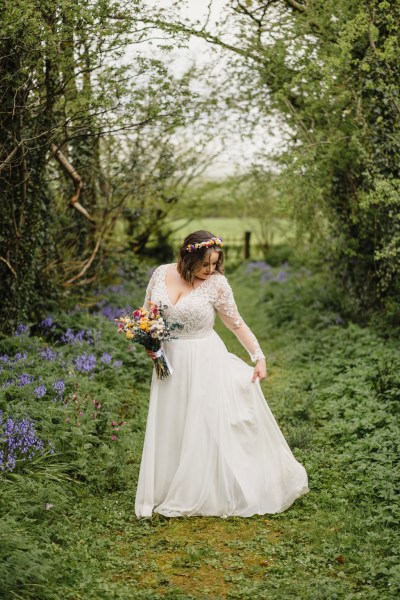 Bride on her own stands on the green grass in forest setting