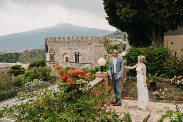 bride and groom at top of wedding venue balcony all smiles celebrating building and landscape in background